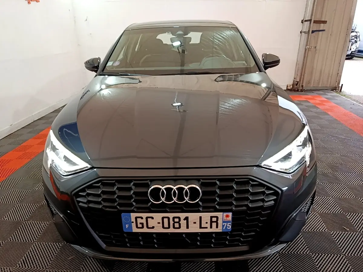 Vue avant d'une Audi A3 gris foncé avec calandre noire et phares LED allumés dans un garage.