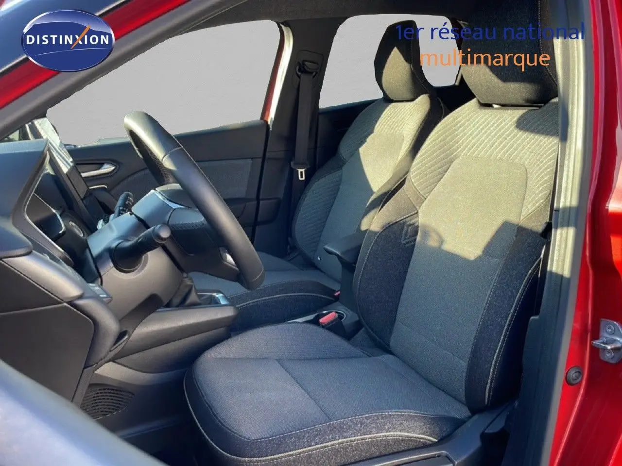 Vue intérieure côté conducteur du Renault Captur rouge désir métal, montrant les sièges tissu gris et le volant cuir noir.