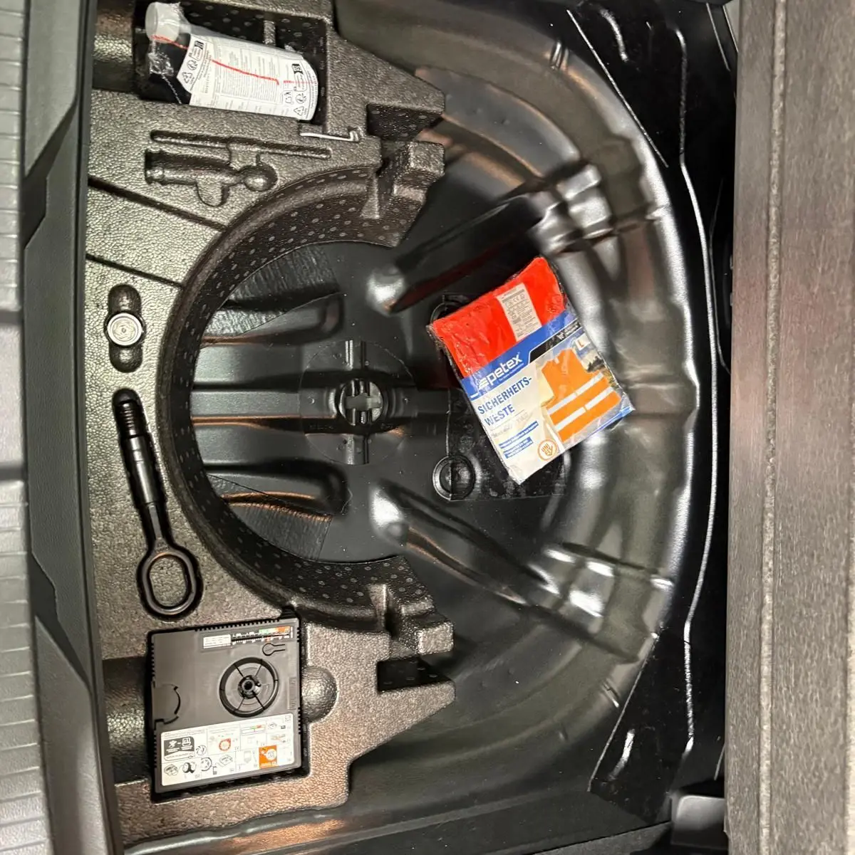 Coffre ouvert montrant le rangement noir du Volkswagen T-Roc 1.5 TSI 2025 avec kit de sécurité et espace pour roue de secours.