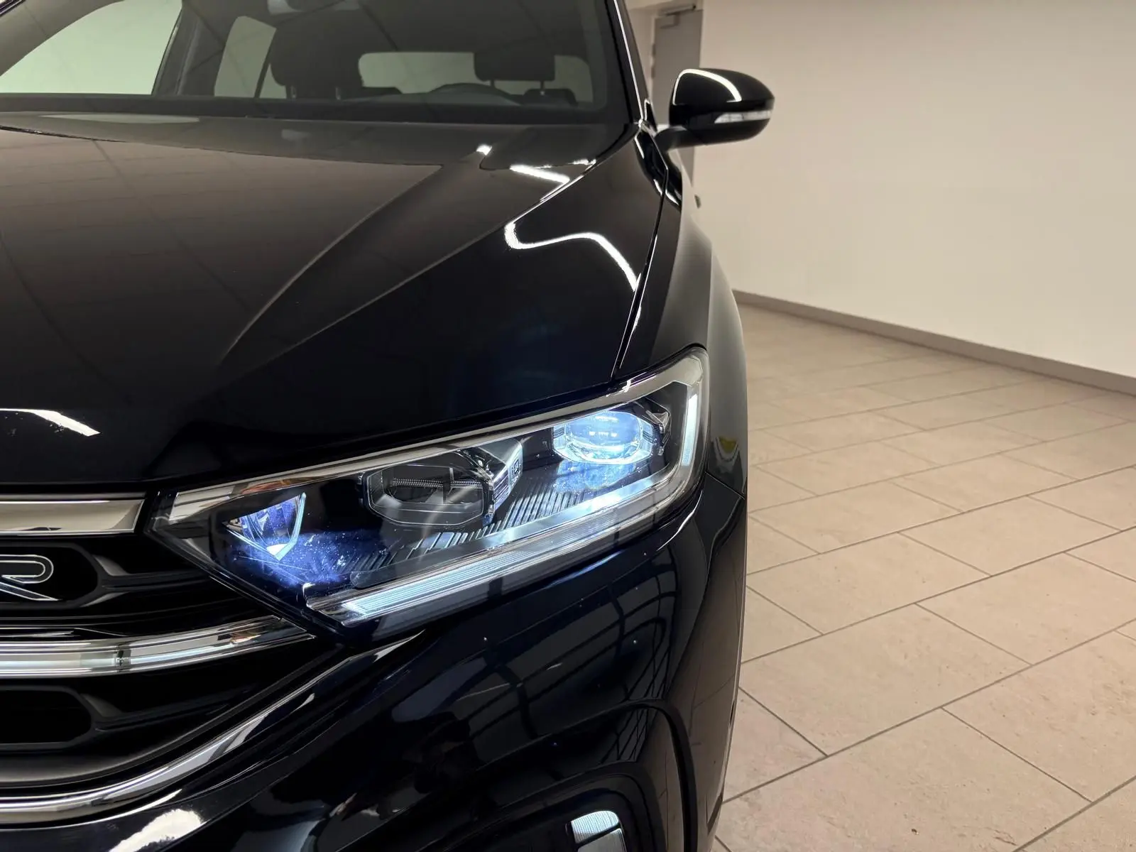 Volkswagen T-Roc noir intense en 3/4 avant droit, avec phares LED allumés et jantes R-Line distinctives.