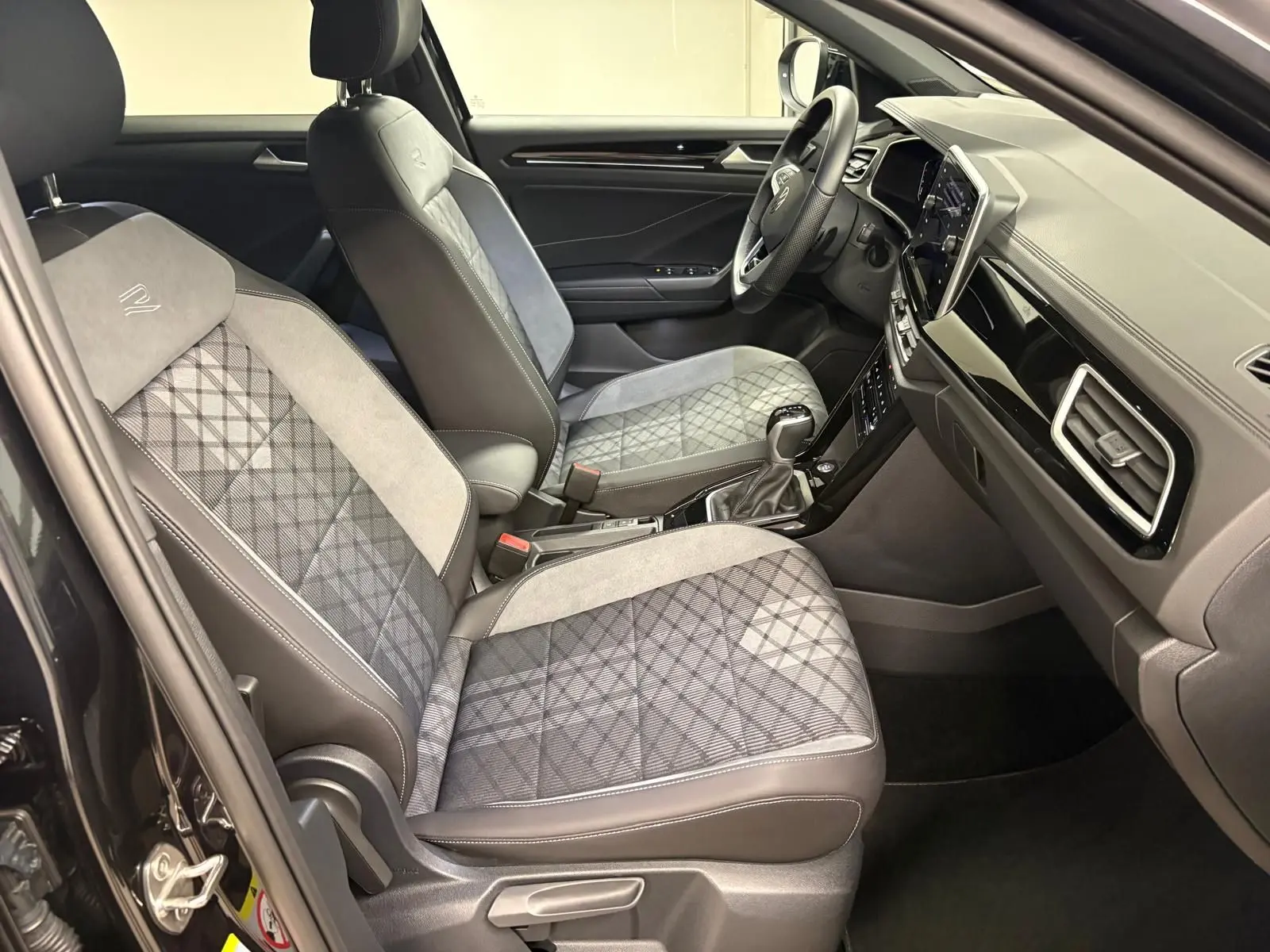 Vue intérieure côté conducteur du Volkswagen T-Roc 1.5 TSI R-Line 2025 avec sièges tissu et alcantara gris à motifs.