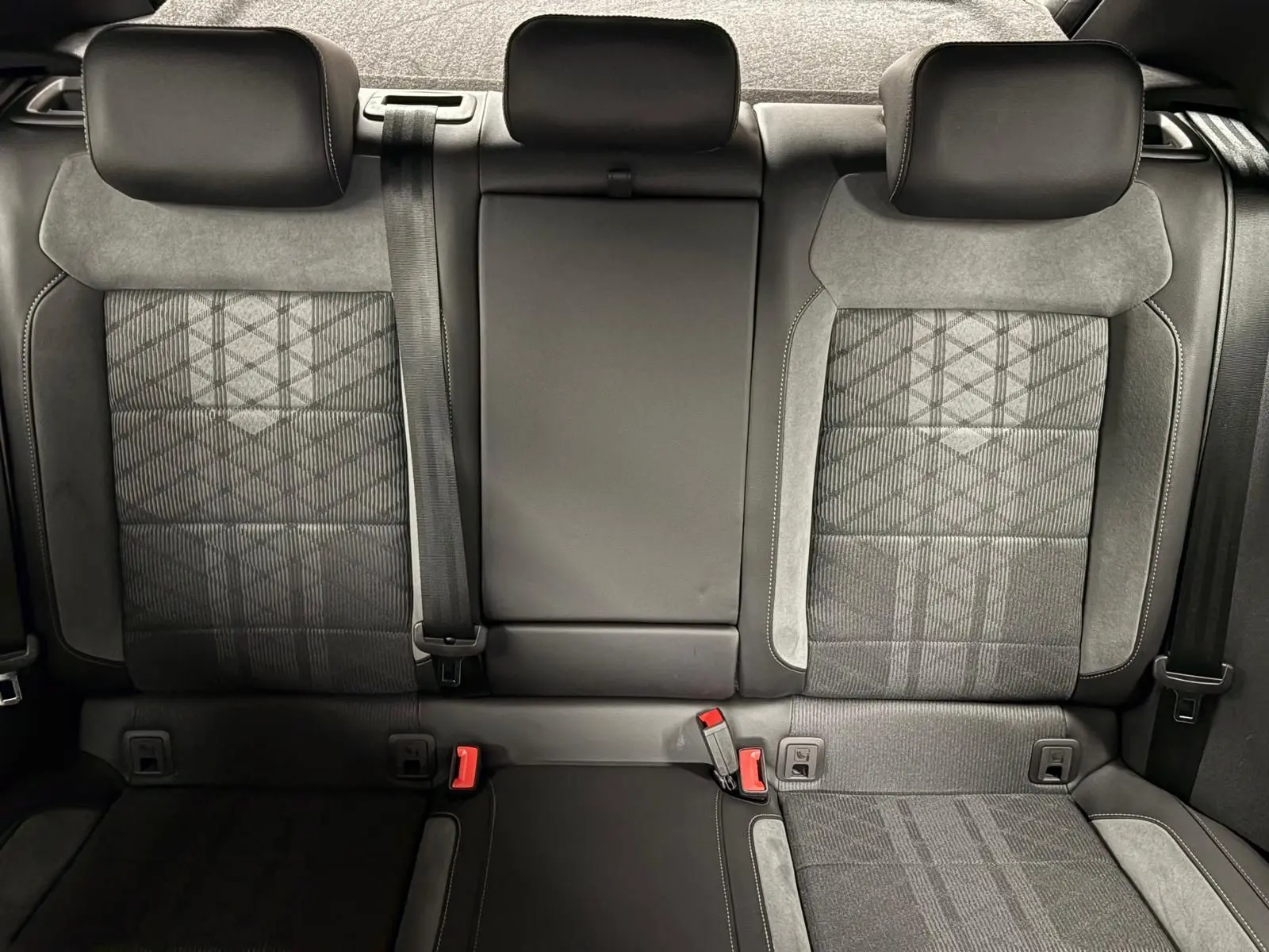 Vue intérieure arrière des sièges arrière du Volkswagen T-Roc 2025, tissu gris à motifs avec appuie-têtes et ceintures visibles.