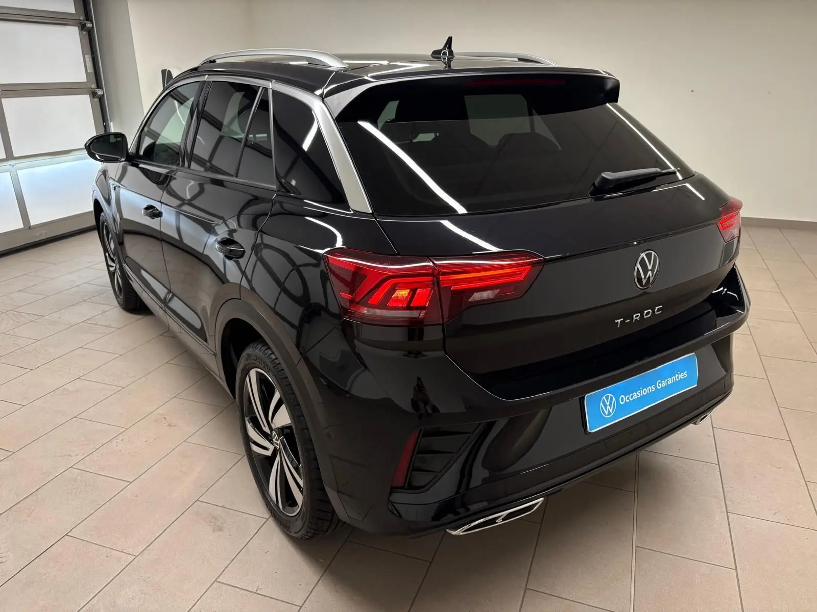 Vue 3/4 arrière droite du Volkswagen T-Roc noir intense 2025 avec feux arrière allumés et jantes R-Line visibles.