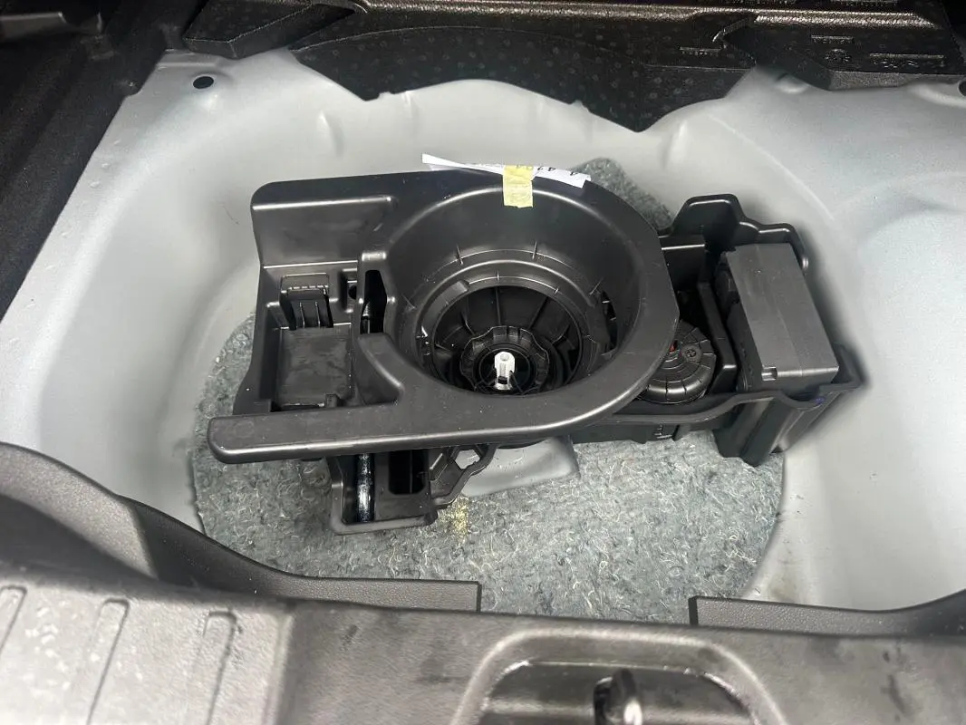 Gros plan sur le rangement de la roue de secours dans le coffre du Jeep Avenger 2025, structure plastique noire et fond gris clair.