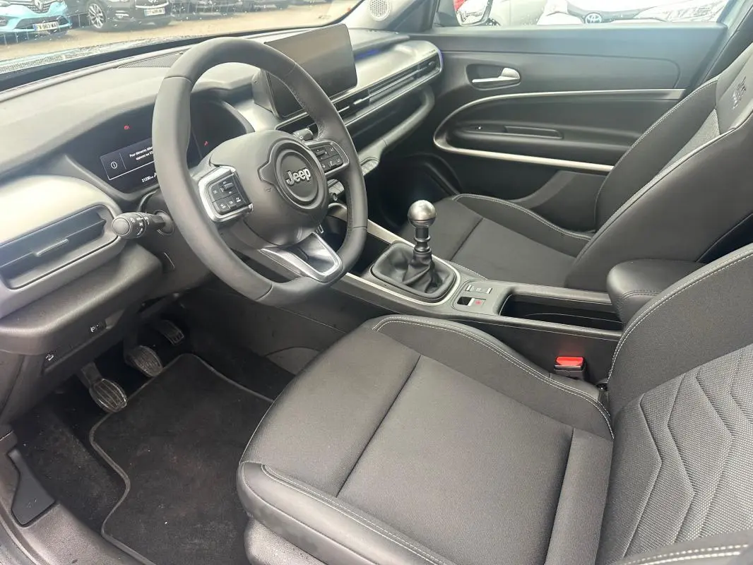 Vue intérieure côté conducteur du Jeep Avenger 2025, volant cuir, boîte manuelle, sièges noirs avec surpiqûres blanches.