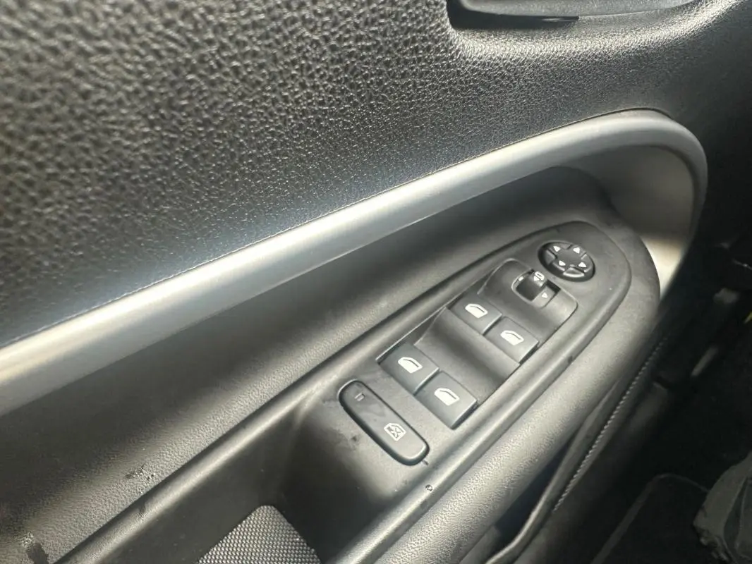 Gros plan sur les commandes électriques des vitres et des rétroviseurs côté conducteur du Jeep Avenger gris foncé 2025.