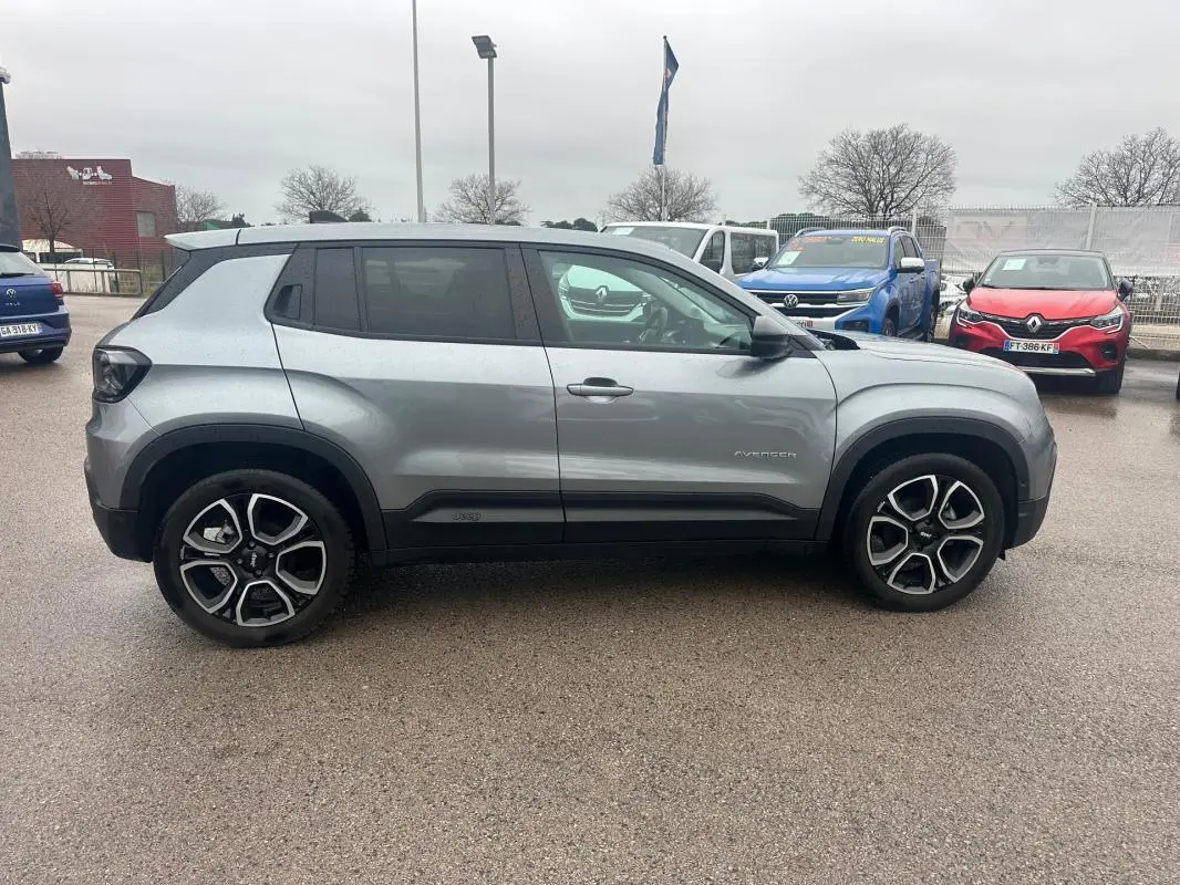 Vue de profil côté gauche d'un Jeep Avenger gris foncé avec jantes alliage 18 pouces sur parking extérieur.