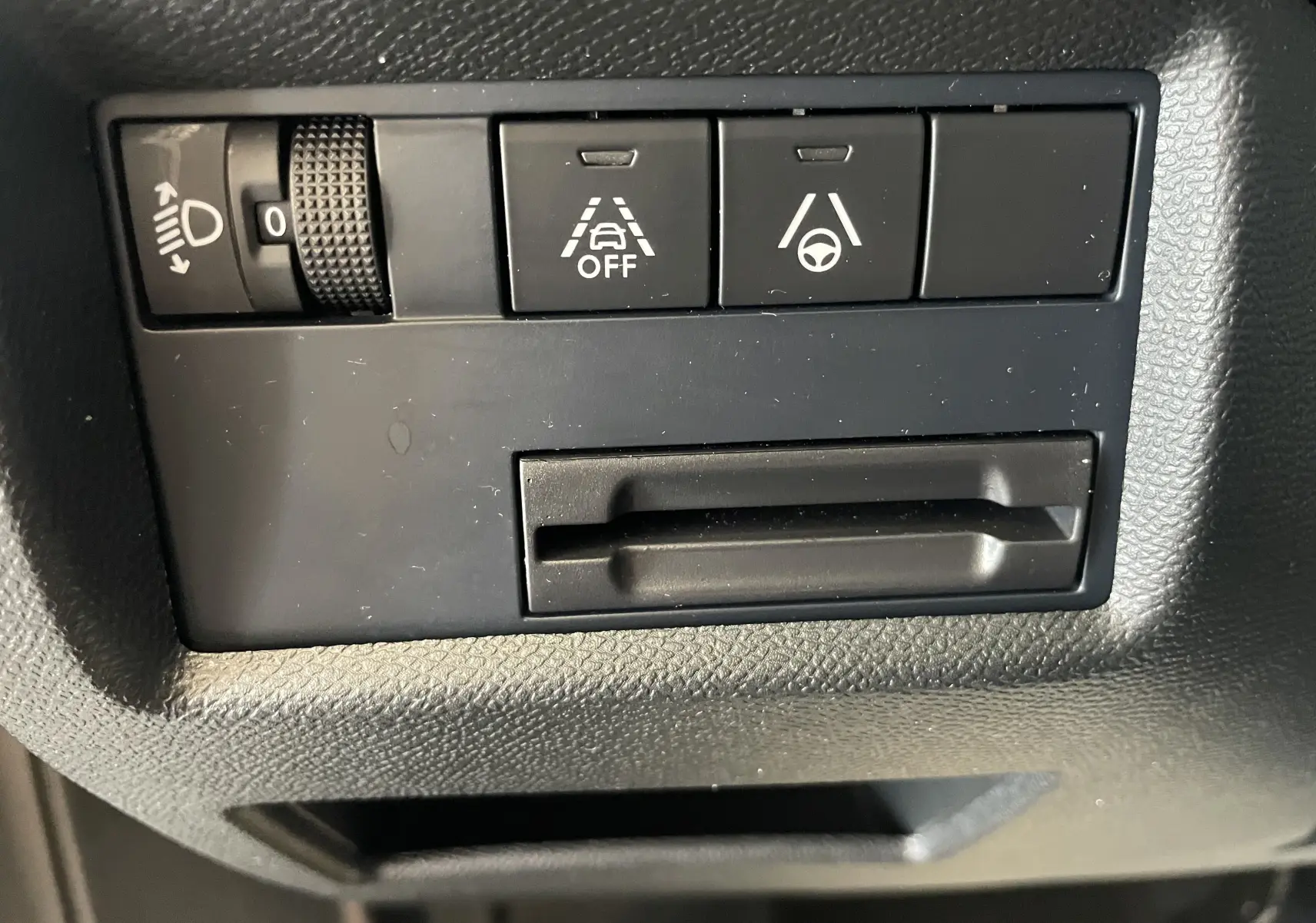 Gros plan sur les commandes noires du tableau de bord du Citroën C5 Aircross hybride 2025, avec réglage des phares et aides à la conduite.