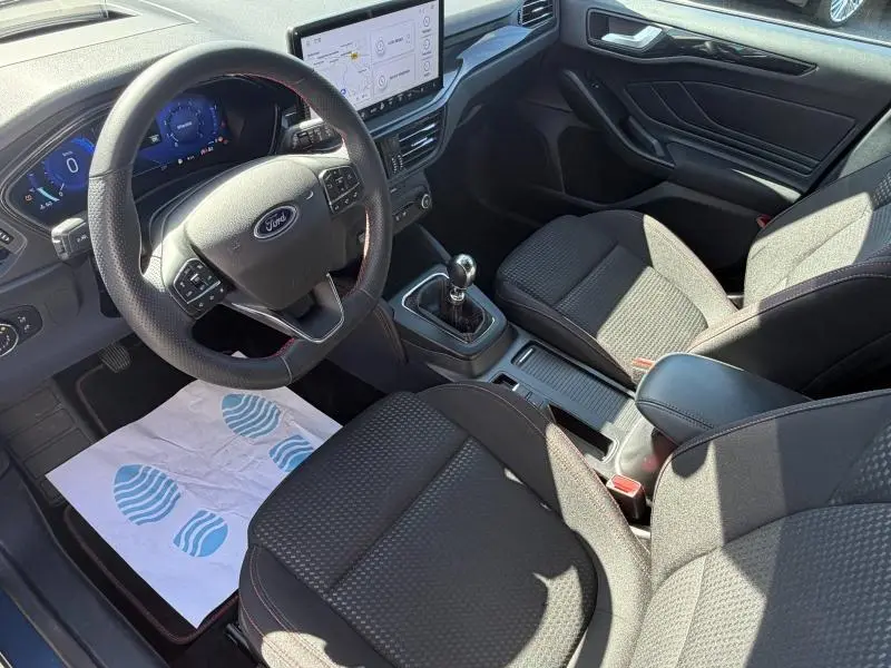 Vue intérieure côté conducteur de la Ford Focus SW 2023, volant multifonction, boîte manuelle et sièges noirs tissu.