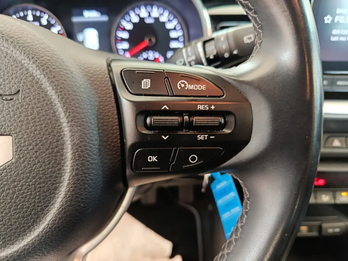 Gros plan sur le volant cuir noir du Kia Stonic 2023, avec commandes multifonctions et tableau de bord lumineux en arrière-plan.