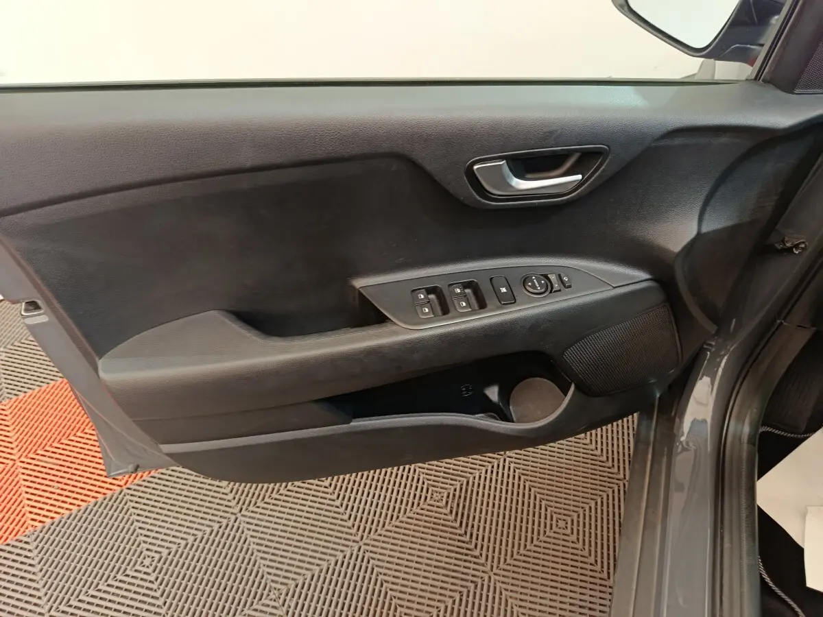 Vue rapprochée de la porte avant gauche grise du KIA STONIC 2023 avec commandes électriques et poignée intérieure chromée.