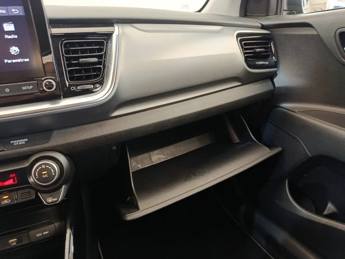 Intérieur KIA Stonic 2023 vue côté passager, tableau de bord gris clair avec boîte à gants ouverte.