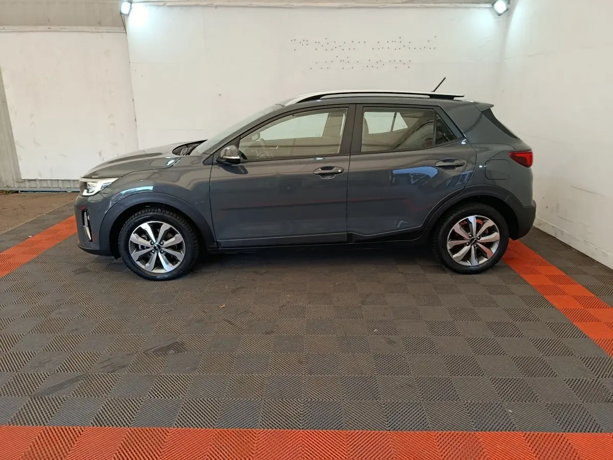 KIA Stonic gris foncé vu de profil côté gauche dans un garage avec sol à damier gris et rouge.