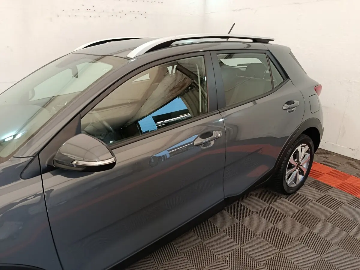 Vue latérale gauche d'un KIA STONIC gris foncé avec barres de toit blanches et jantes alliage.