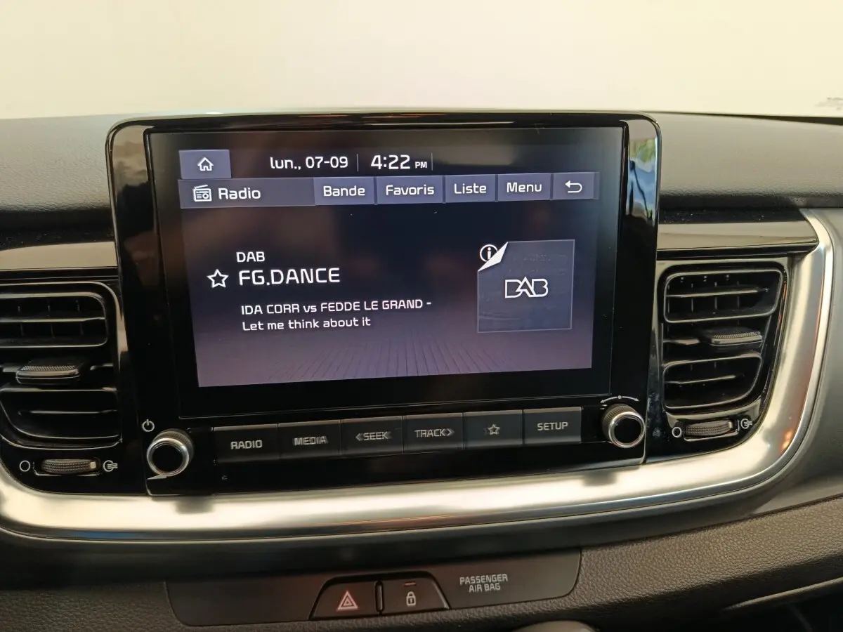 Écran tactile central de la Kia Stonic 1.0 T-GDI 2023 affichant une station radio DAB, entouré de grilles d'aération noires.