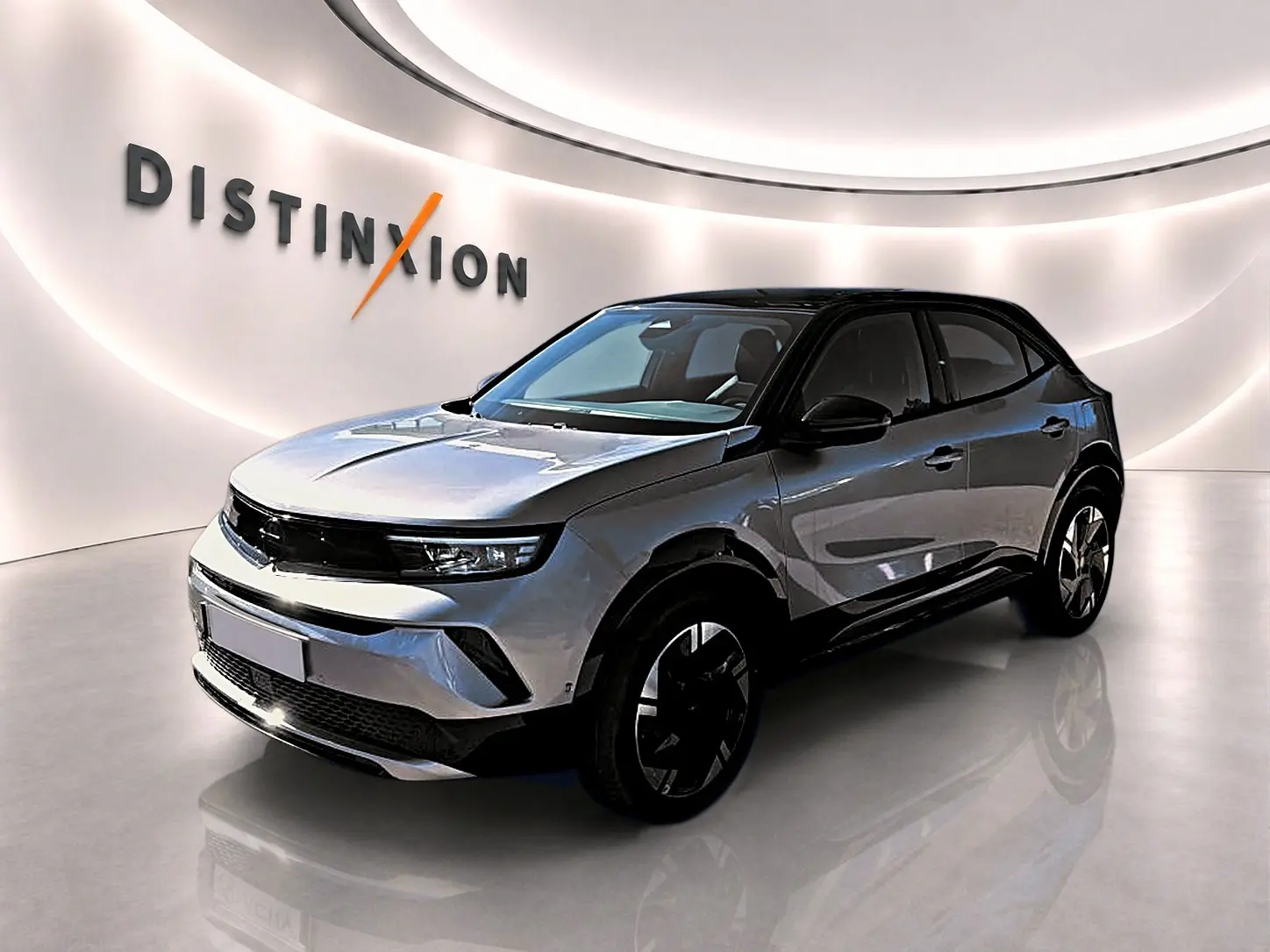 Opel Mokka Electric gris en 3/4 avant droit, avec toit noir et jantes alu distinctives dans un showroom lumineux.