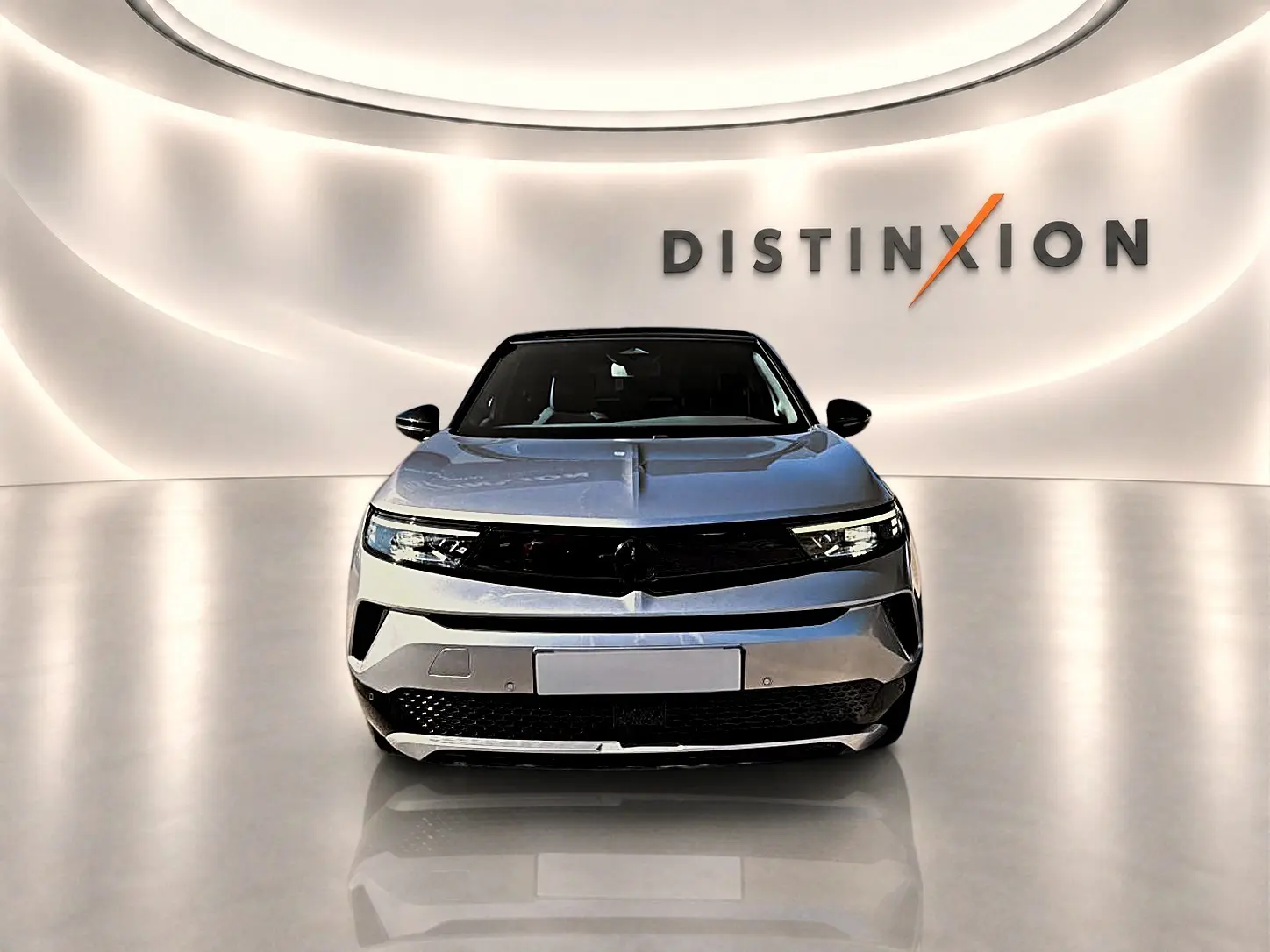 Vue frontale d'un Opel Mokka Electric gris 2025, avec calandre noire et éclairage LED, sur fond lumineux "Distinxion".