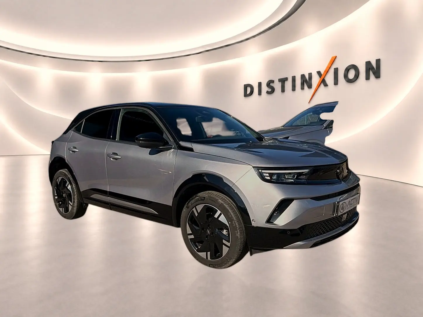 Opel Mokka Electric gris en 3/4 avant droit, avec jantes noires et toit contrasté noir dans un showroom lumineux.