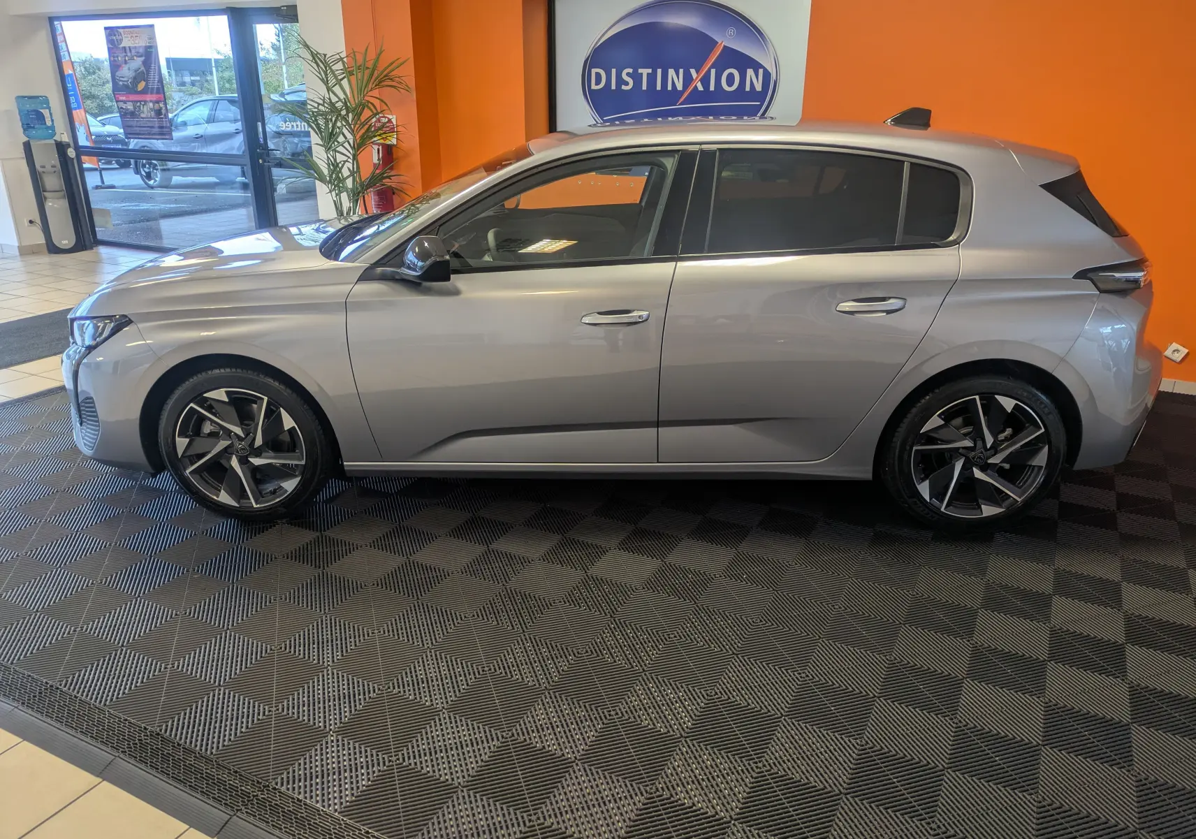 Peugeot 308 gris Artense vue de profil côté gauche dans un showroom avec jantes alliage distinctives.