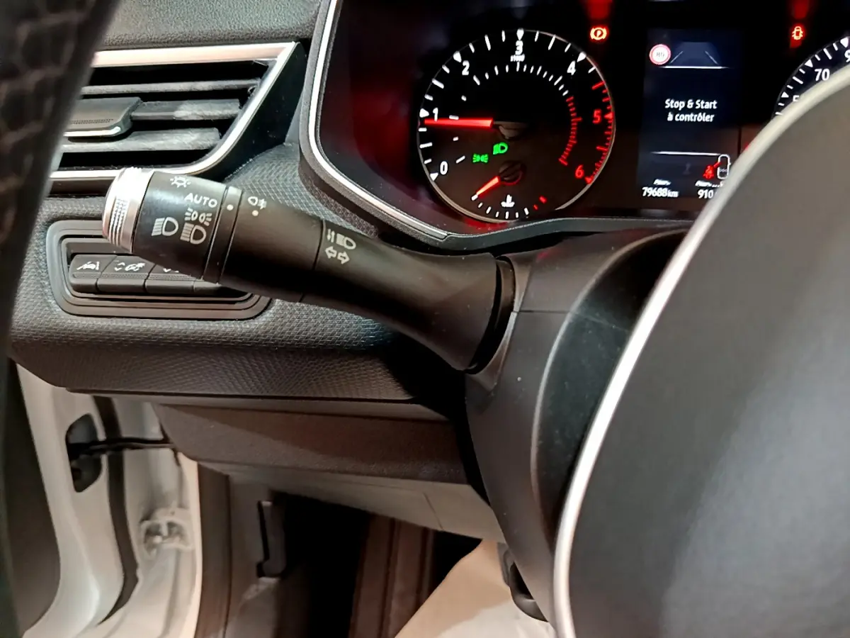 Gros plan sur la manette des phares et clignotants à gauche du volant d'une Renault Clio Business Blue dCi 85 blanche, tableau de bord visible.