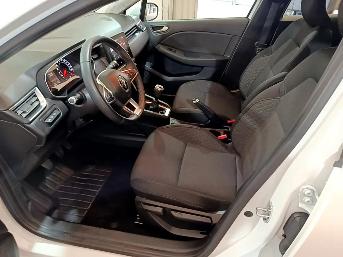 Intérieur côté conducteur d'une Renault Clio Business blanc, volant cuir, sièges tissu gris et tableau de bord moderne.