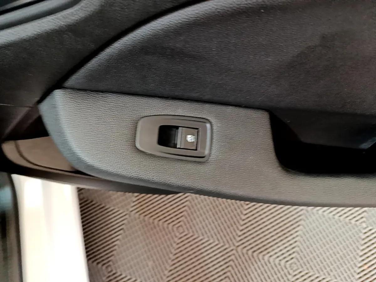 Bouton de commande de lève-vitre sur la porte intérieure côté conducteur d'une Renault Clio Business Blue dCi 85 blanche.