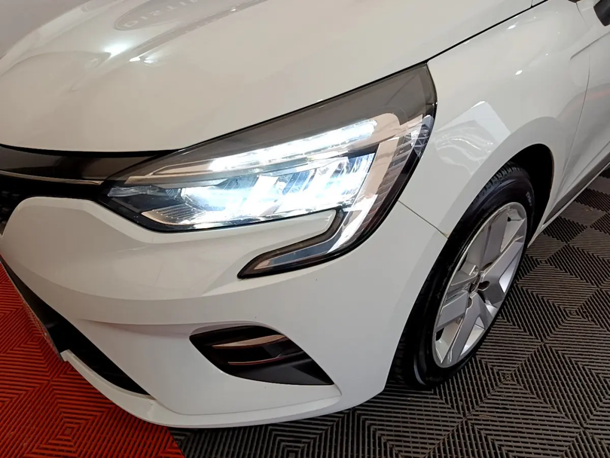 Gros plan sur l'avant droit blanc d'une Renault Clio 2020 avec phare LED allumé et jante alliage visible