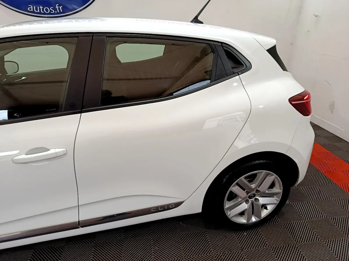 Vue latérale côté droit d'une Renault Clio blanche avec jante alliage et logo Clio sur la bas de porte arrière.