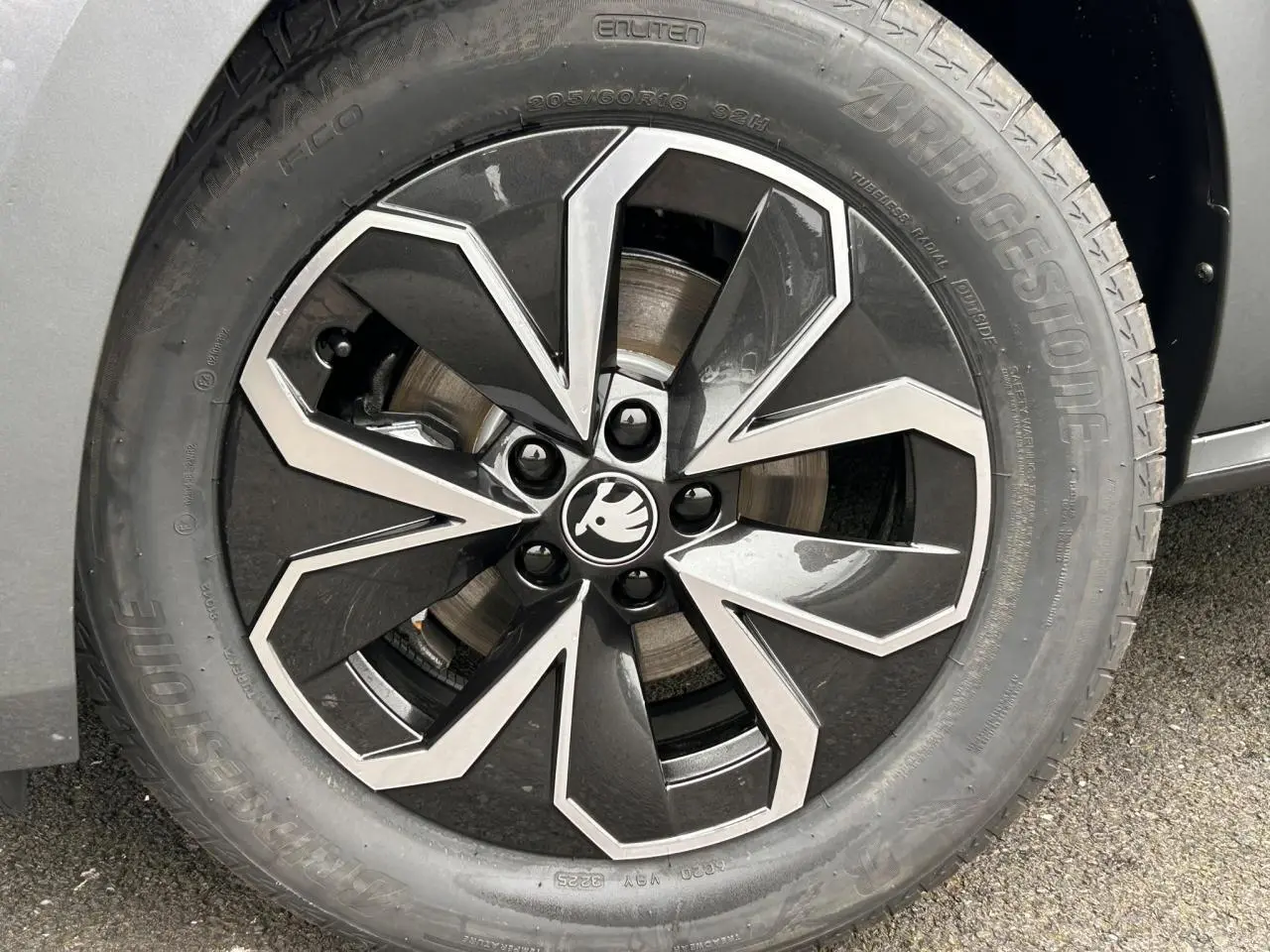 Gros plan sur la jante alliage 16 pouces bicolore du côté gauche d’un Skoda Kamiq gris graphite, avec logo central noir et blanc.