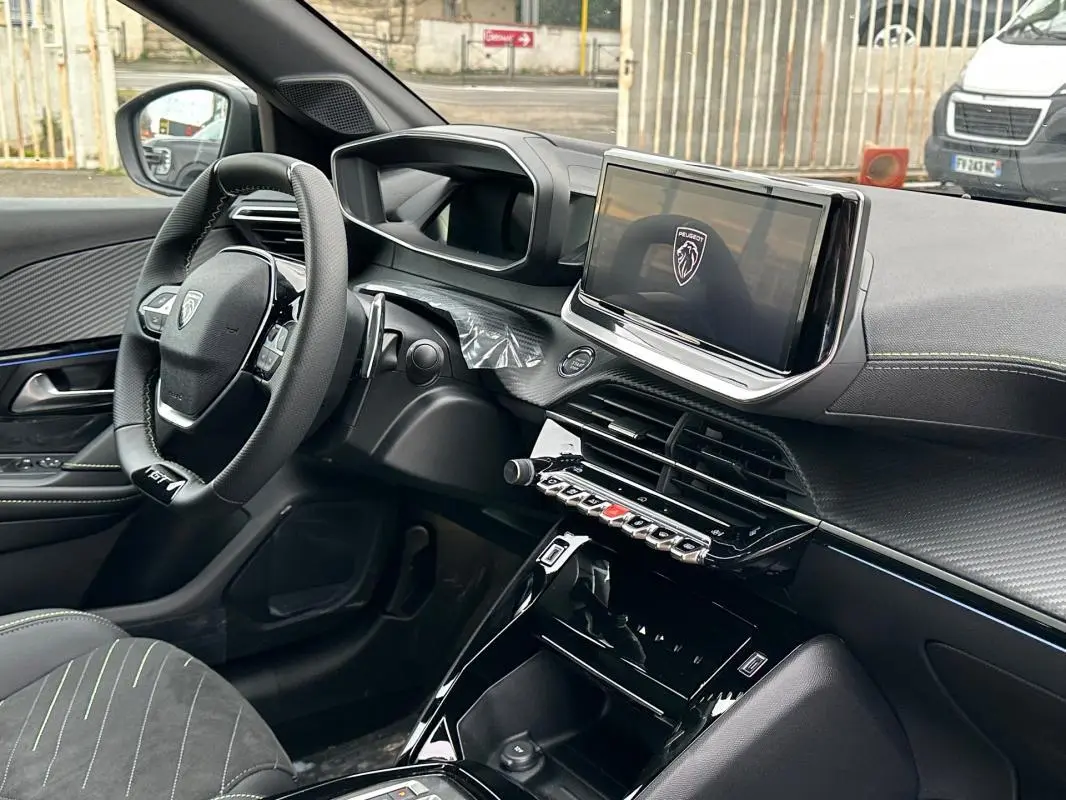 Vue intérieure côté conducteur du Peugeot 208 Hybrid 110 gris, mettant en valeur le volant GT, l'écran tactile et la finition moderne du tableau de bord.