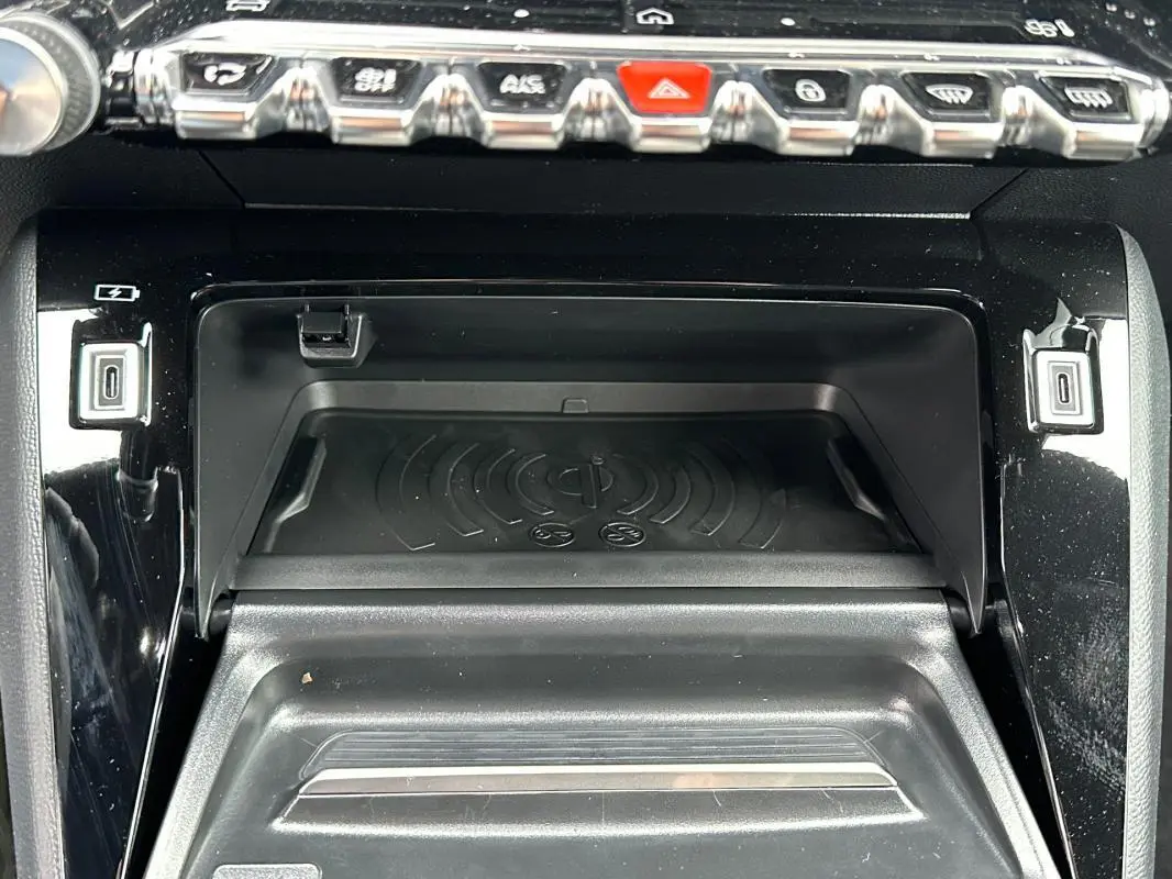 Vue rapprochée de la console centrale noire du Peugeot 208 Hybrid 110 e-DCS6 GT avec zone de recharge sans fil et commandes chrome.