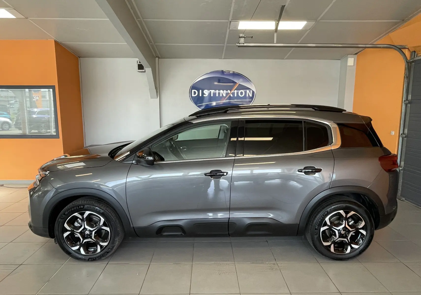 Vue de profil côté gauche du Citroën C5 Aircross hybride gris platinium avec jantes alliage 18 pouces biton en intérieur showroom.