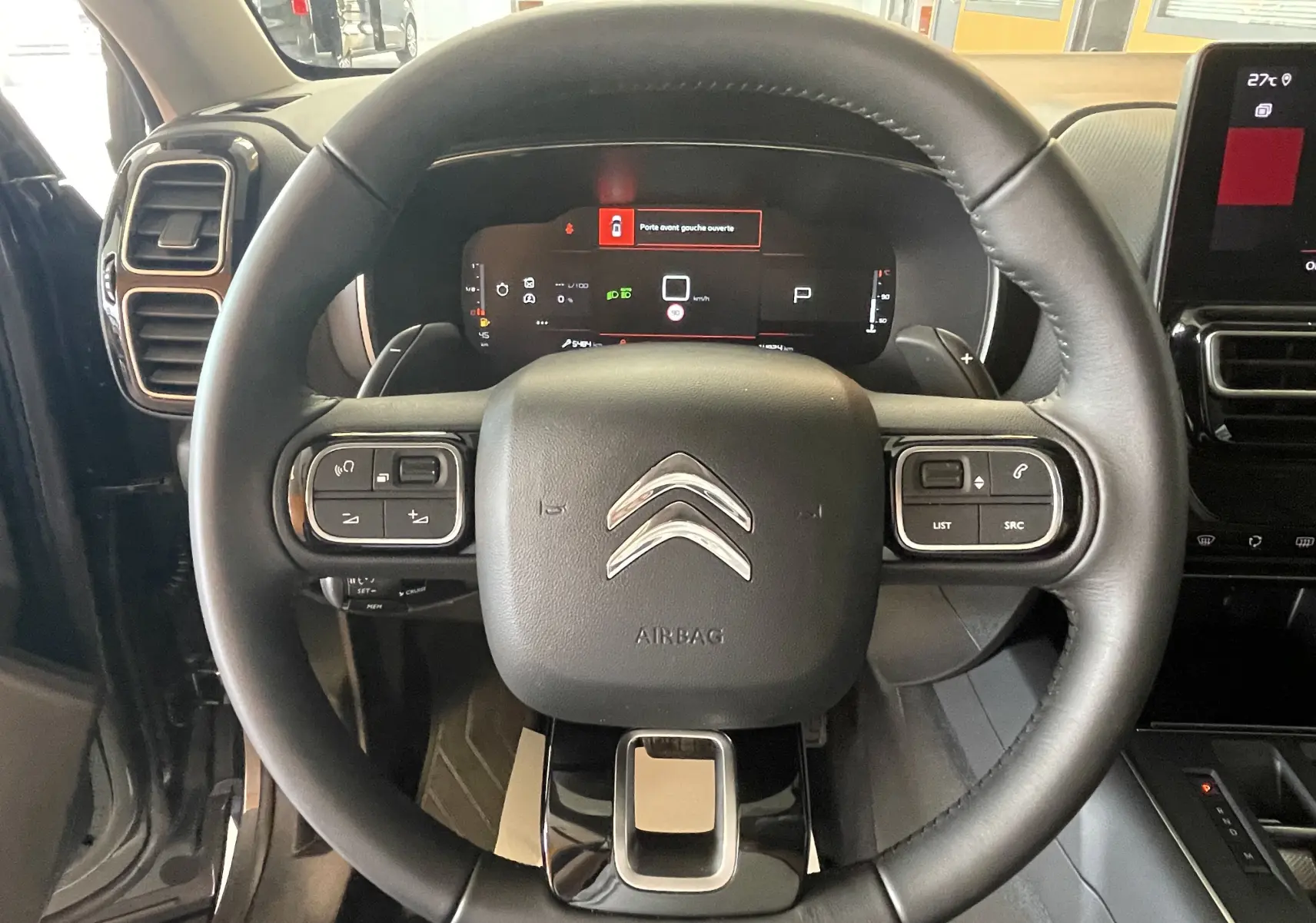 Vue rapprochée du volant en cuir noir du Citroën C5 Aircross gris platinium, avec tableau de bord digital et commandes intégrées.