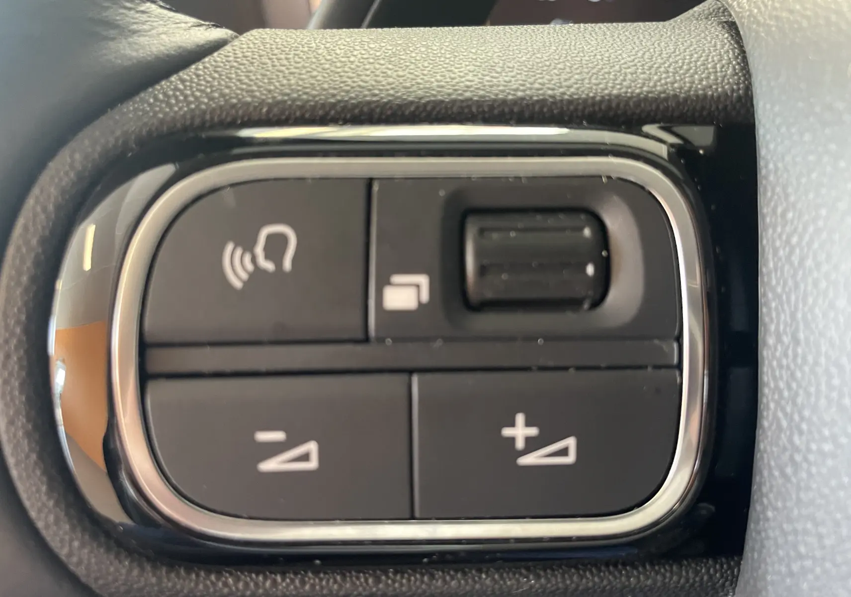 Gros plan sur les commandes au volant du Citroën C5 Aircross hybride 2025, boutons noirs avec symboles blancs.