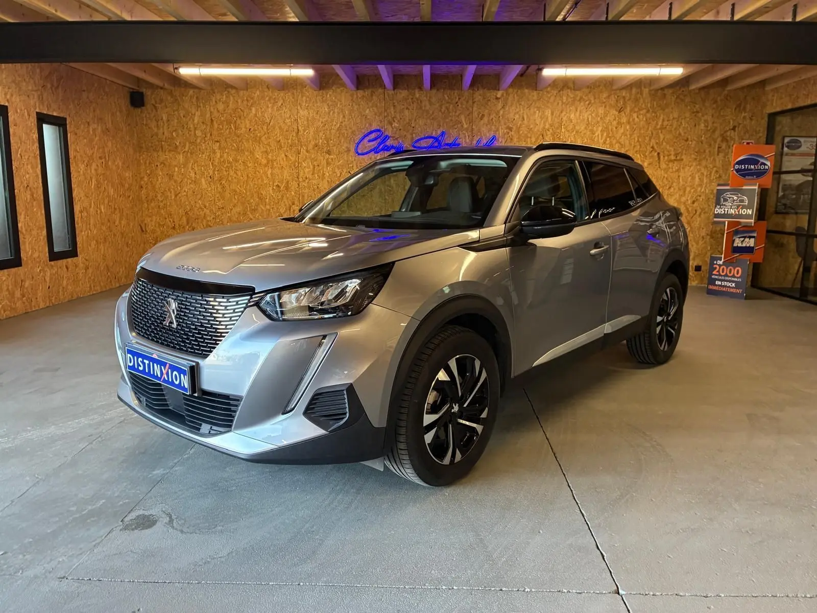 Peugeot 2008 gris métallisé vue 3/4 avant droit dans un showroom avec jantes noires et toit noir.