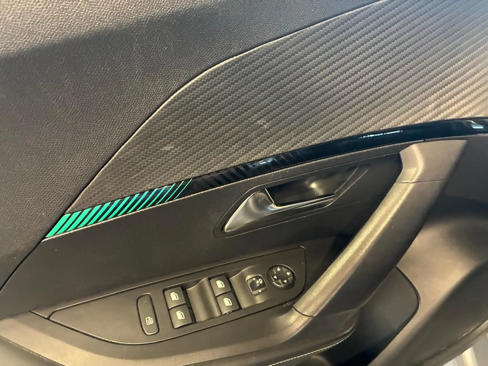 Détail de la porte côté conducteur du Peugeot 2008 gris, avec commandes de vitres et insert décoratif noir à rayures vertes.