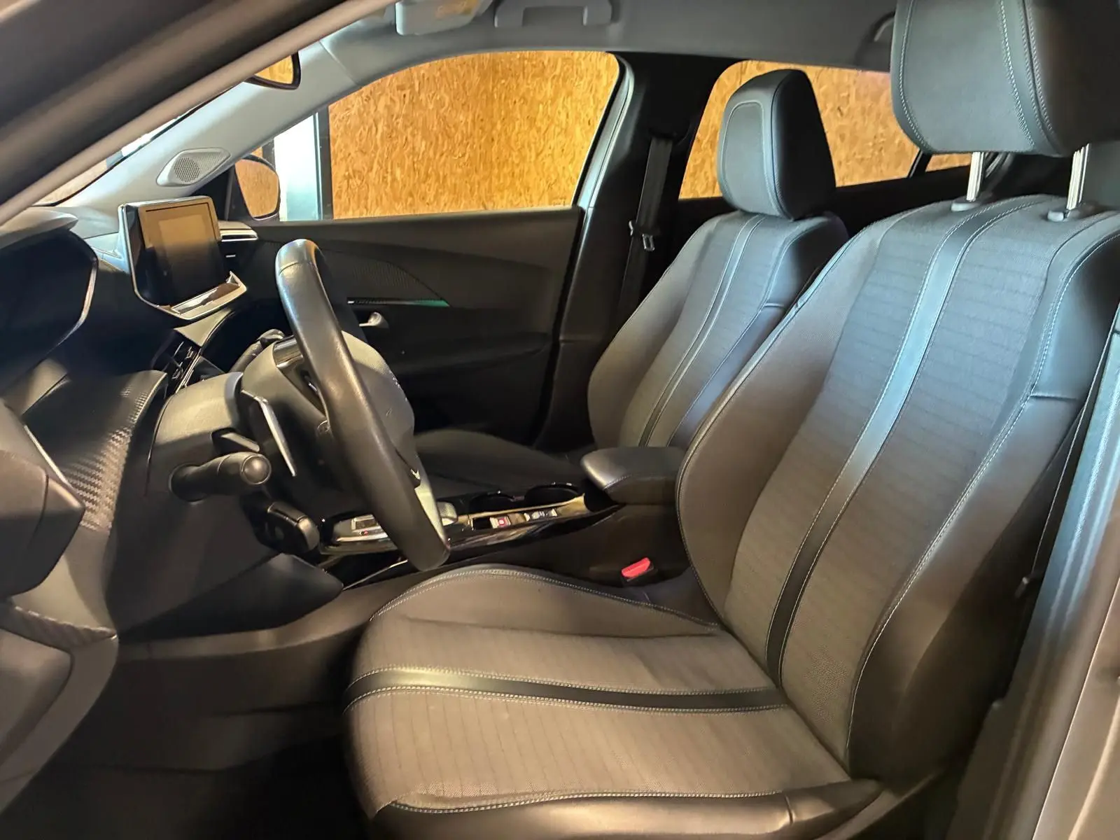 Vue intérieure côté conducteur du Peugeot 2008 2022, sièges en tissu noir et tableau de bord moderne avec écran tactile.