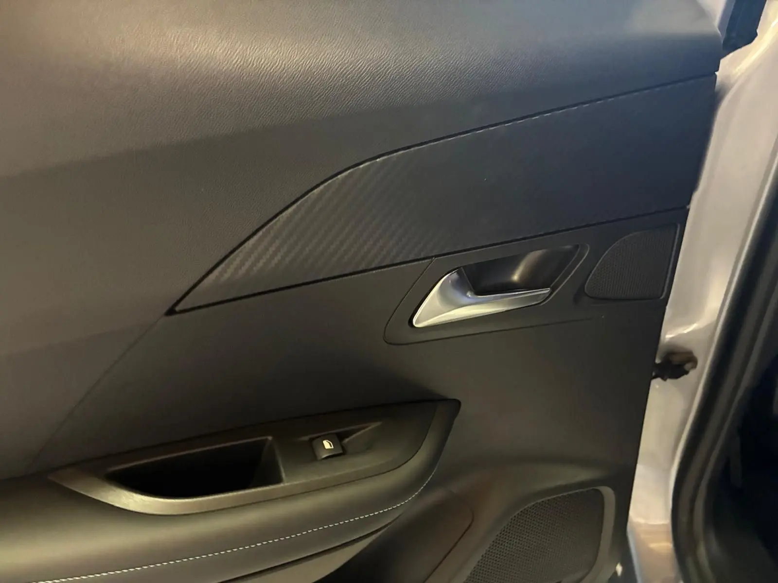 Détail de la porte intérieure côté gauche du Peugeot 2008 gris, avec poignée argentée et insert effet carbone.