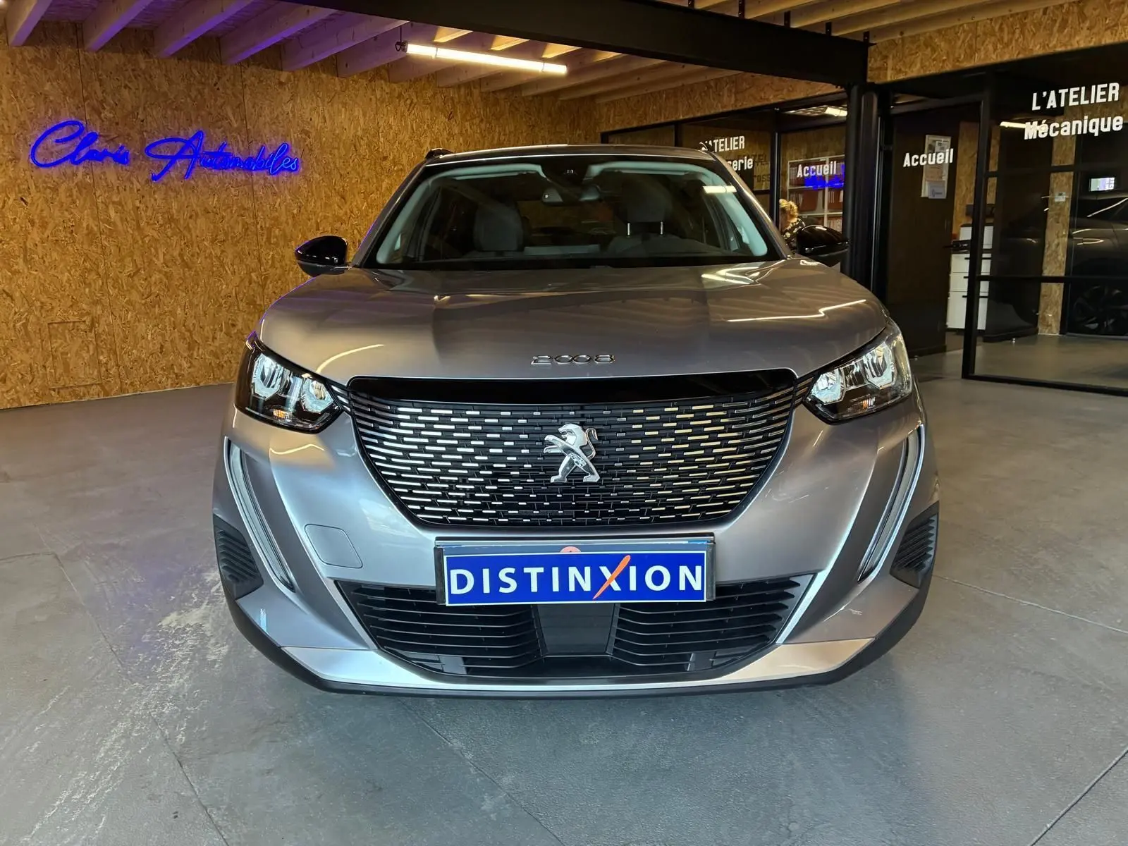 Vue avant d'un Peugeot 2008 gris 2022 avec calandre noire et phares LED allumés en intérieur showroom.