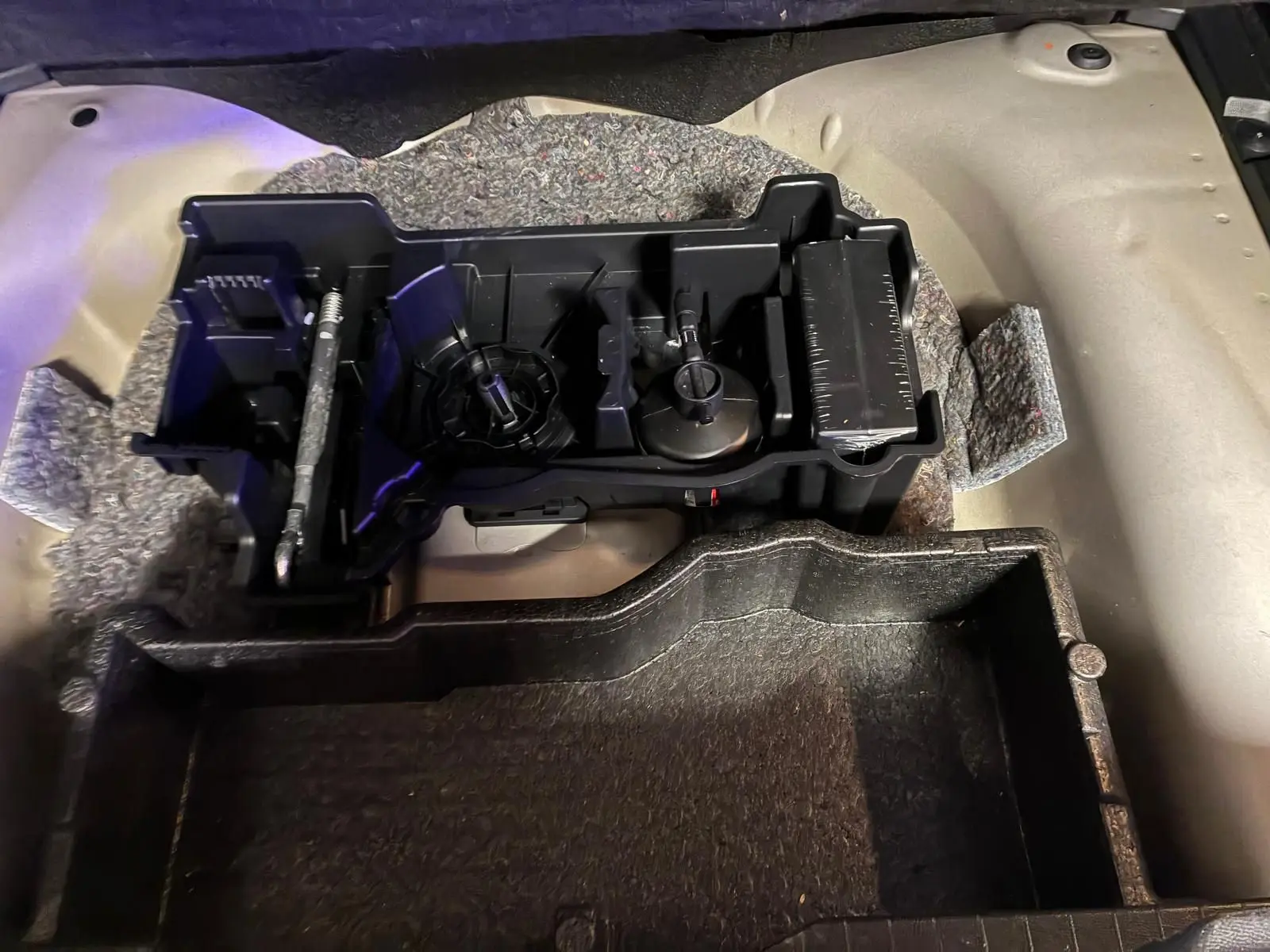 Vue rapprochée du rangement sous le plancher du coffre d'un Peugeot 2008 gris, montrant les compartiments en plastique.