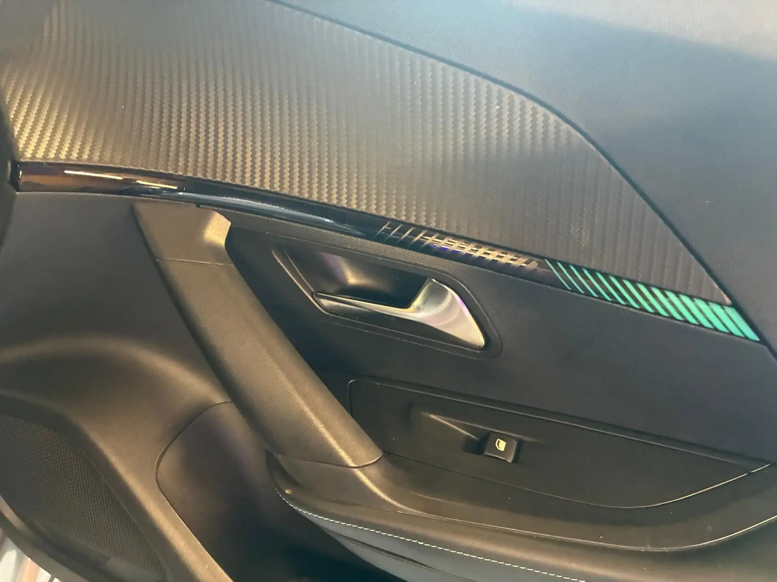 Détail de la porte intérieure côté gauche du Peugeot 2008 gris, avec poignée argentée et insert décoratif noir à motifs verts.