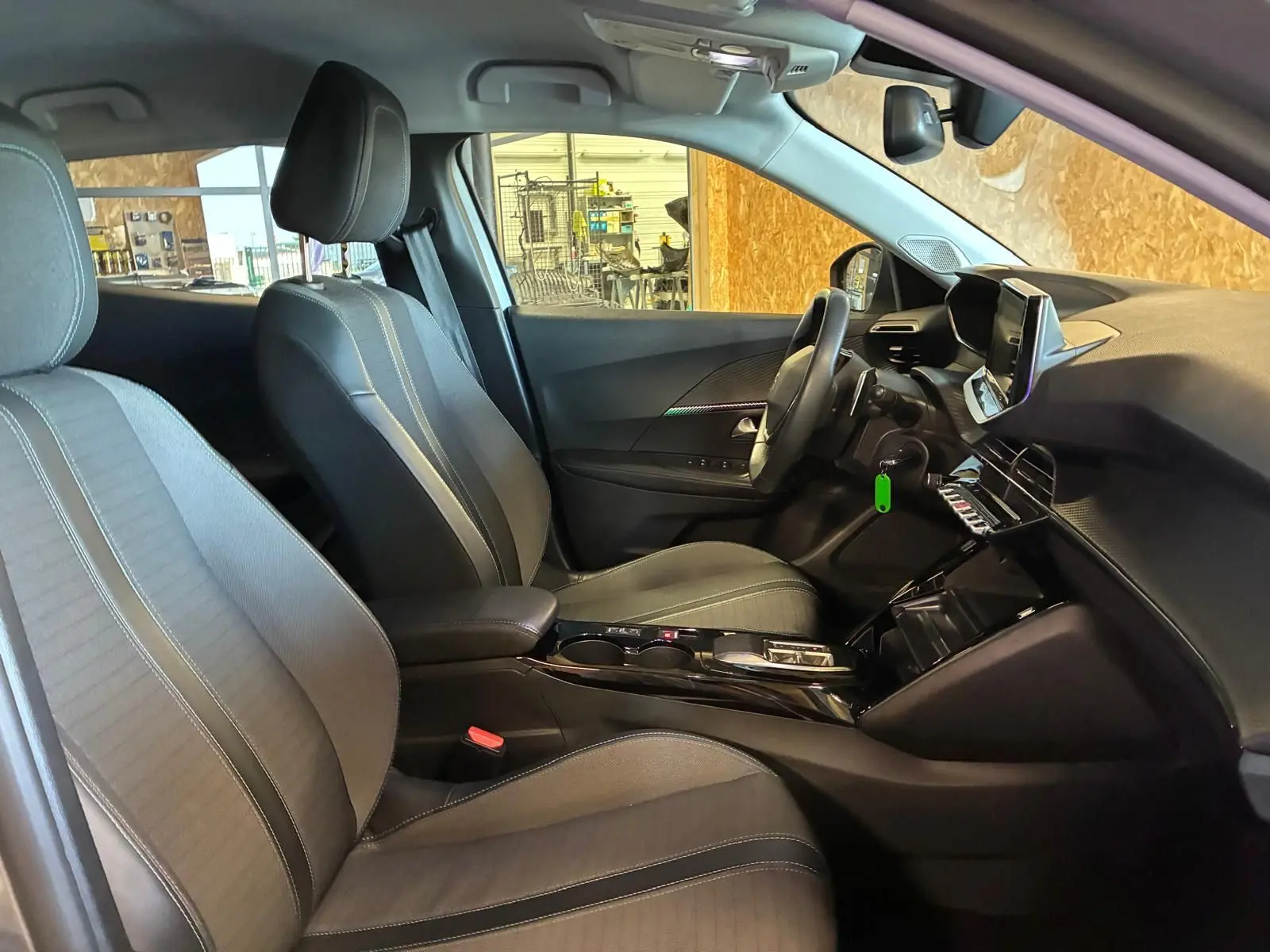 Vue intérieure côté gauche du poste de conduite du Peugeot 2008 gris, mettant en valeur les sièges tissu noirs et la console centrale moderne.