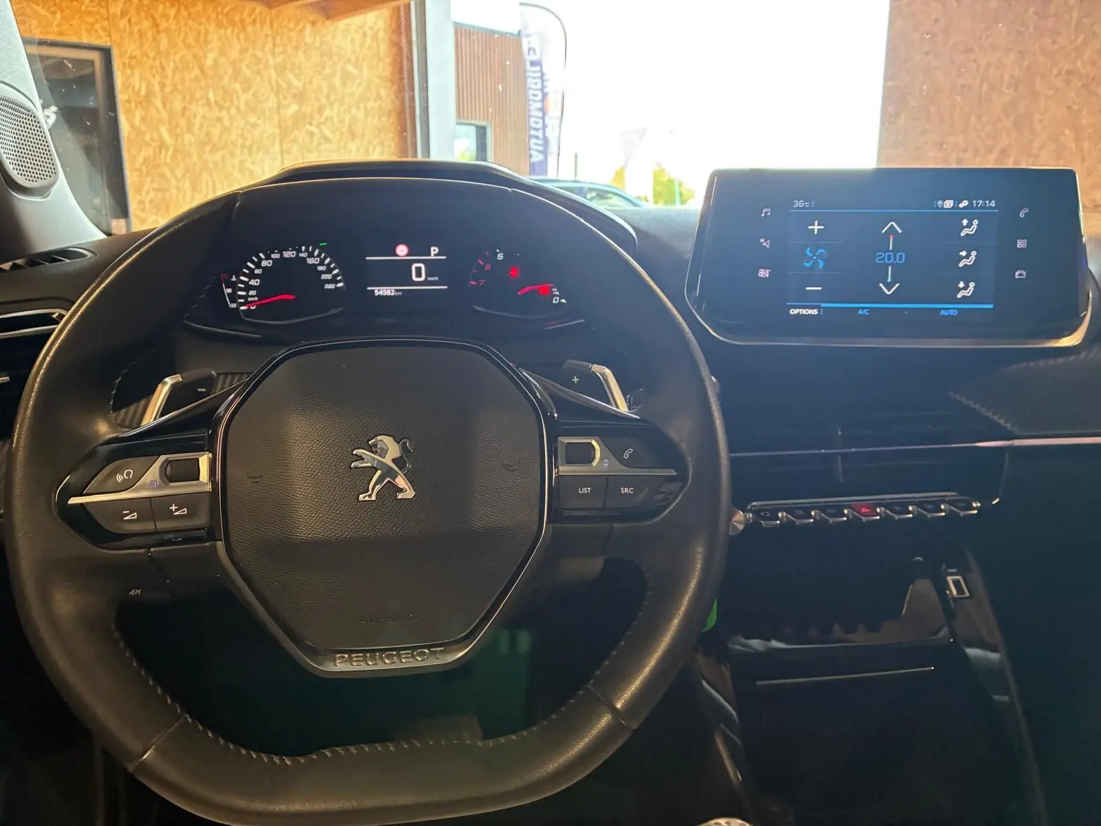Vue intérieure centrée sur le volant noir du Peugeot 2008 2022 avec tableau de bord digital et écran tactile de climatisation.
