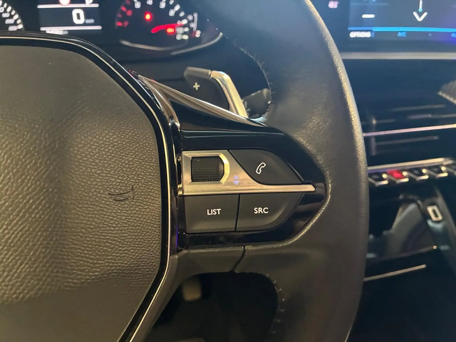 Gros plan sur la partie gauche du volant en cuir noir du Peugeot 2008, avec commandes audio et tableau de bord en arrière-plan.