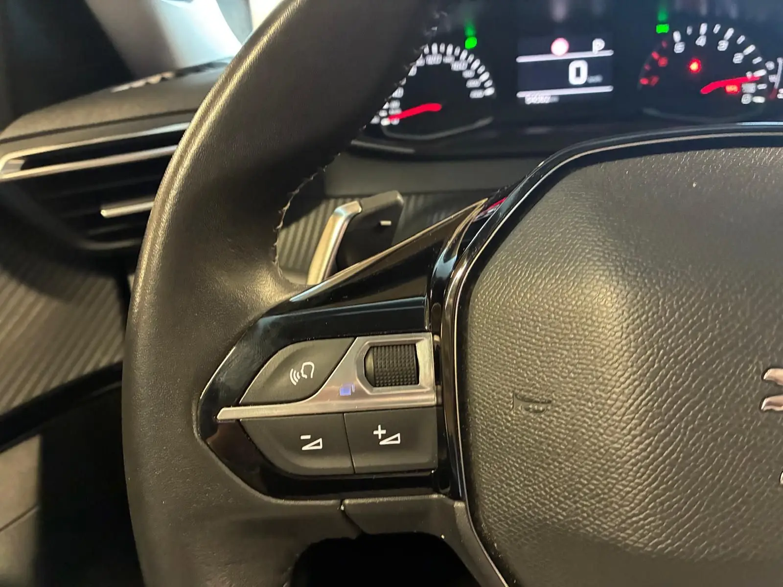 Gros plan sur le volant noir du Peugeot 2008 2022, avec commandes audio et tableau de bord numérique en arrière-plan.