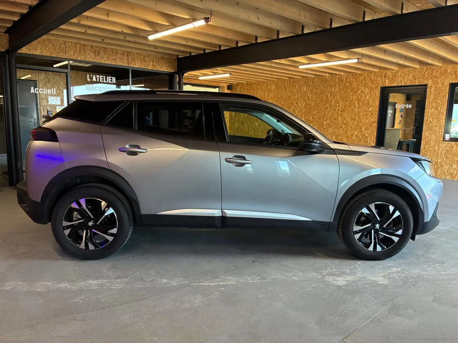 Peugeot 2008 gris vue de profil côté gauche, avec jantes noires et toit noir dans un garage.