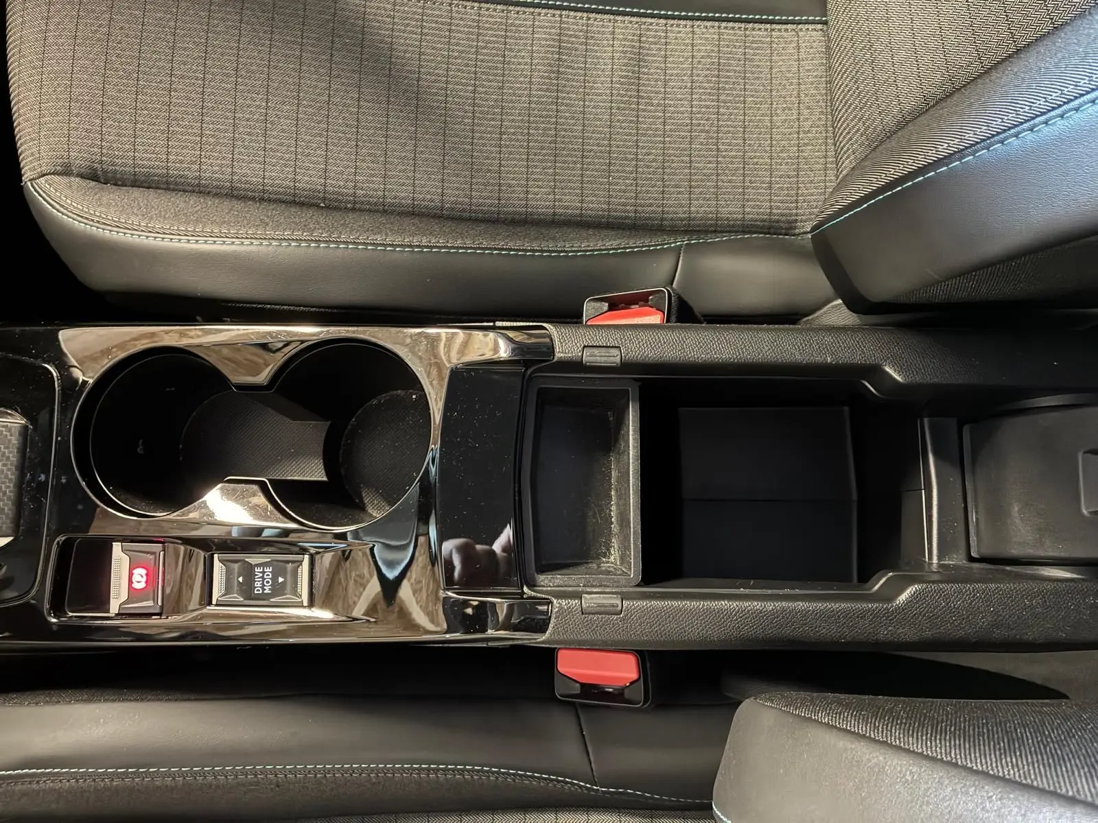 Vue plongeante sur la console centrale noire brillante du Peugeot 2008 1.5 BlueHDi 130, avec porte-gobelets et rangement ouvert.