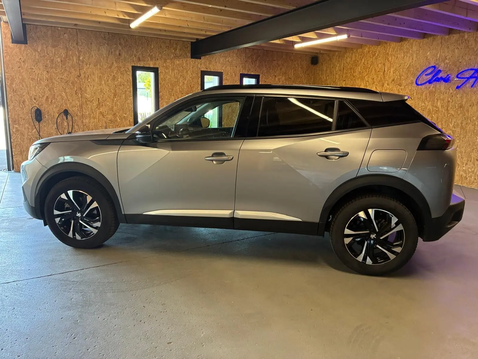 Profil droit d’un Peugeot 2008 gris 2022 avec toit noir et jantes alliage bicolores, stationné en intérieur.