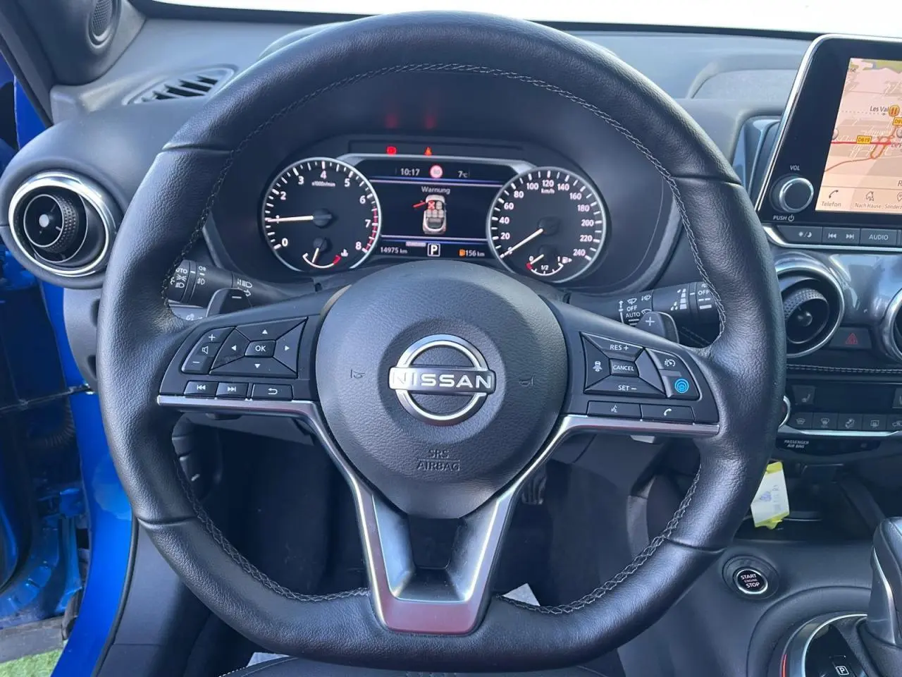 Vue rapprochée du volant en cuir noir du Nissan Juke 2024 bleu magnetic avec tableau de bord digital et écran tactile.