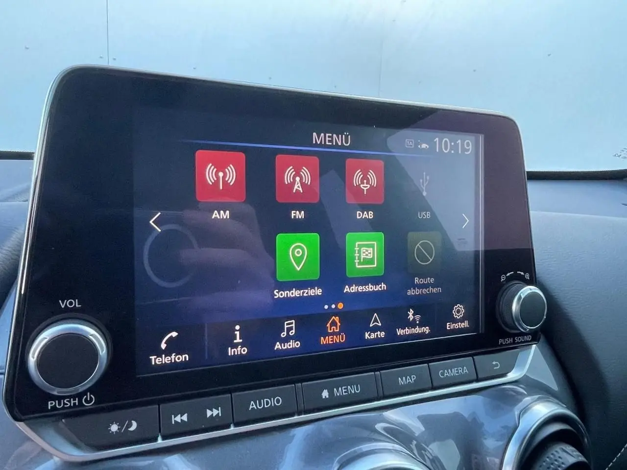 Écran tactile central du Nissan Juke II 2024 affichant le menu multimédia avec commandes autour, intérieur noir.